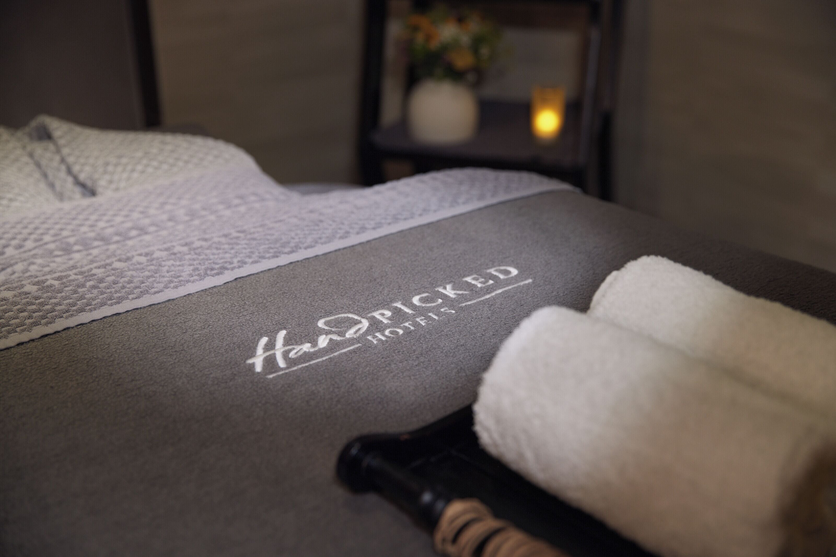 A hotel room with a neatly made bed, a bottle of lotion, and a towel.