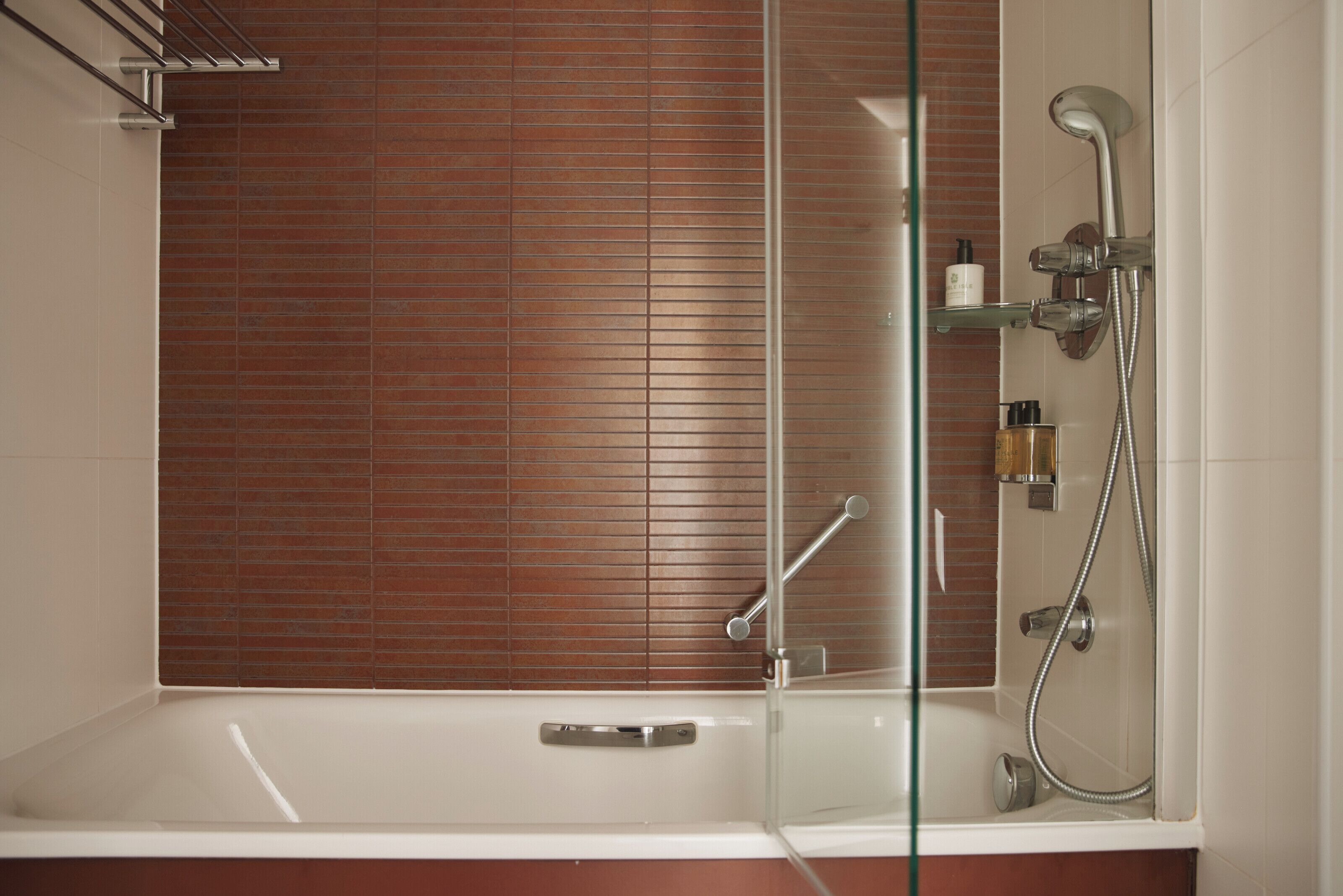 Un baño moderno con ducha envuelta en cristal, una bañera blanca y pared de azulejos.