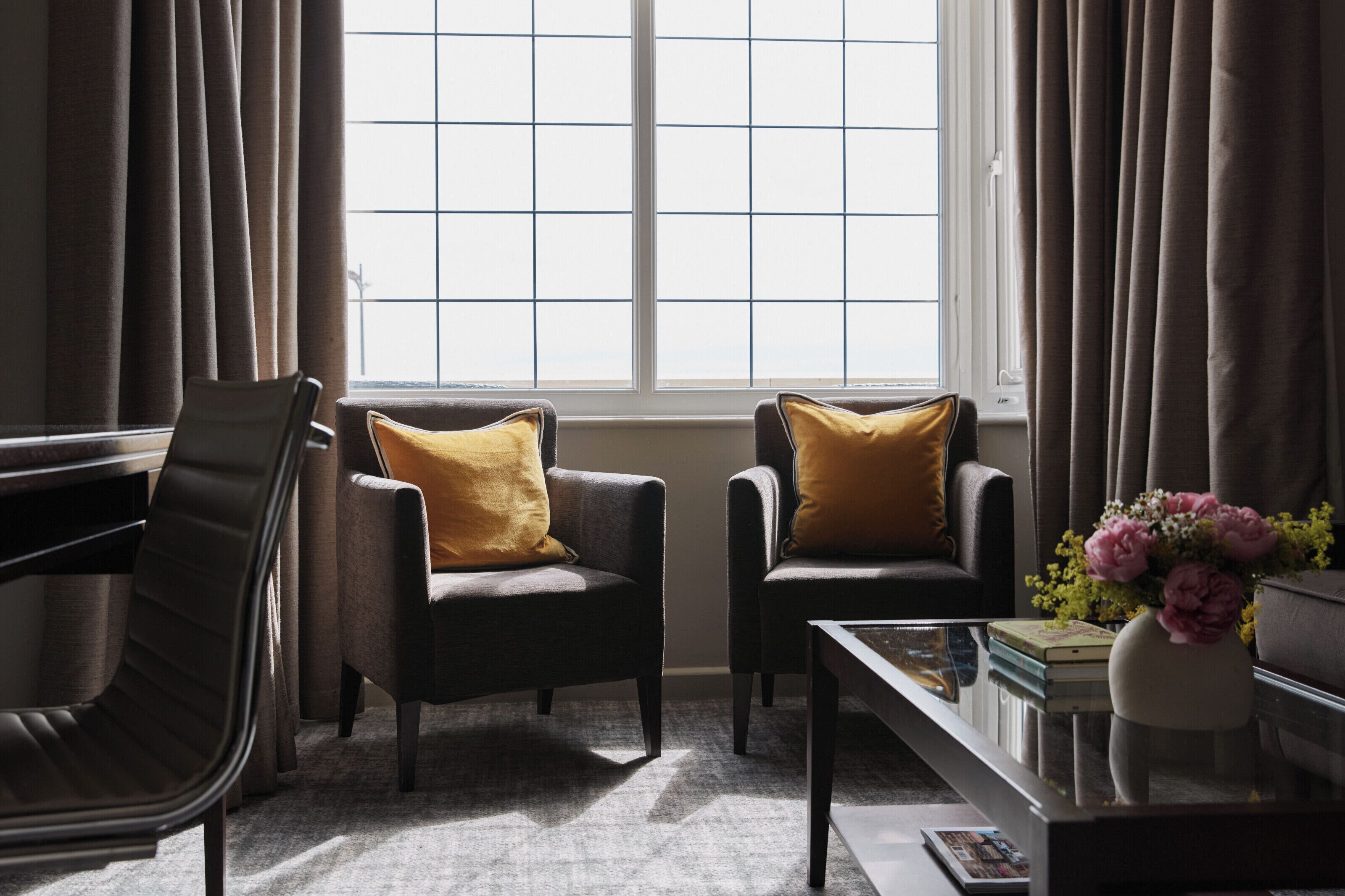 Une pièce avec deux fauteuils, une table basse et une fenêtre avec des rideaux.