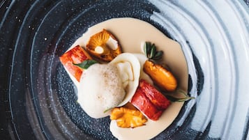 A dessert on a dark plate with a creamy sauce, fruit pieces, and a dollop of cream.