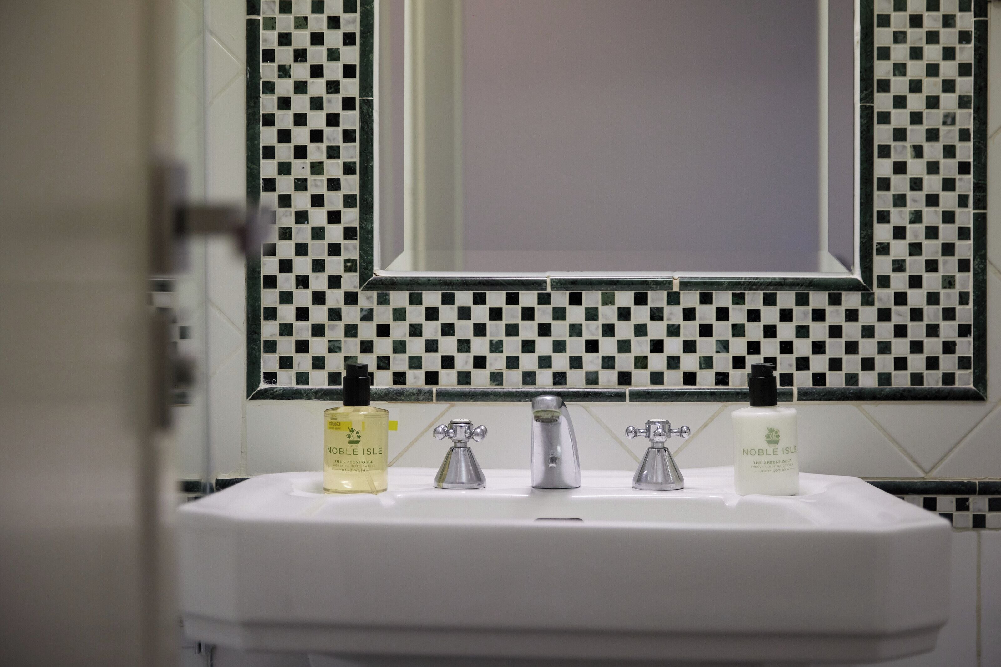 Un baño con salpicadero de azulejos a cuadros, un lavabo blanco y dos botellas de gel de ducha Noble Isle.