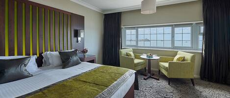 A hotel room with a large bed, two armchairs, a small table, and a view of the sea through a large window.