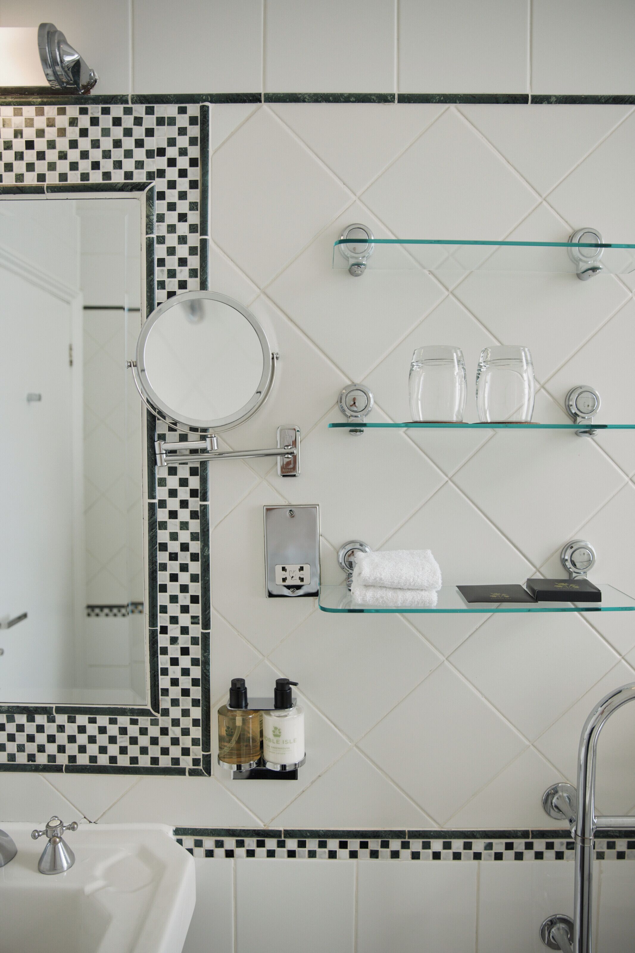 A bathroom with a mirror, glass shelves, a towel rack, and toiletries.