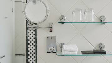 A bathroom with a mirror, glass shelves, a towel rack, and toiletries.
