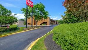 A red sign for a Red Roof Inn, a brick building with a covered walkway, and a well-maintained roadside with a hedge. - Red Roof Inn Edgewood (Edgewood)