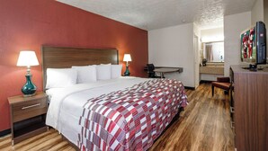 A hotel room with a bed, two bedside lamps, a desk with a chair, a television, and a bathroom visible through an open door. - Red Roof Inn Edgewood (Edgewood)