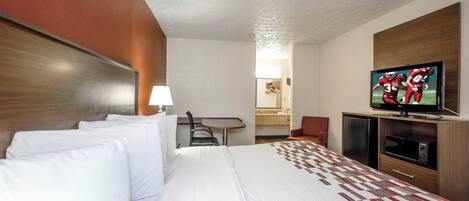 A hotel room with a large bed, a television, a desk, and a mirror.