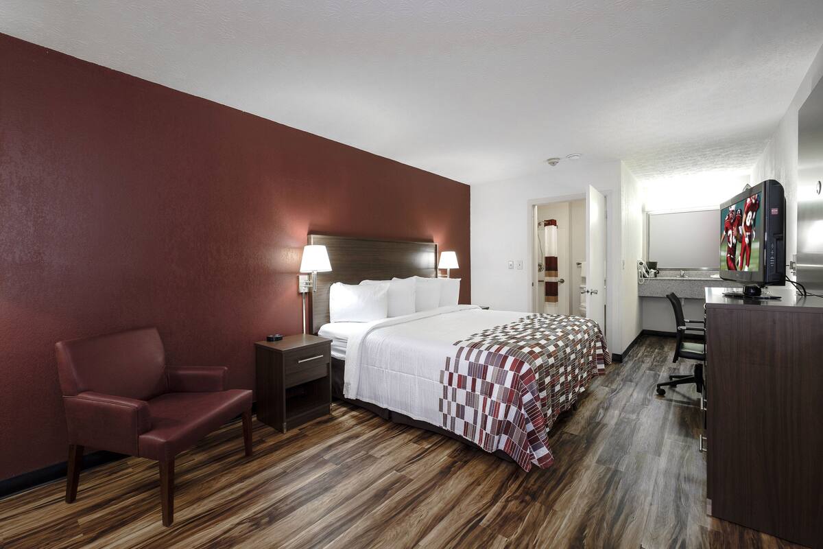 A hotel room with a bed, a desk, a chair, and a television.