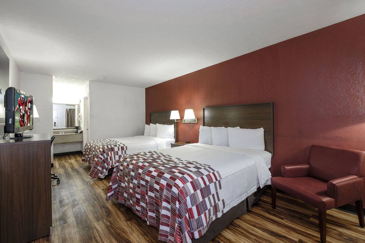 A hotel room with two beds, a desk, a chair, and a television.