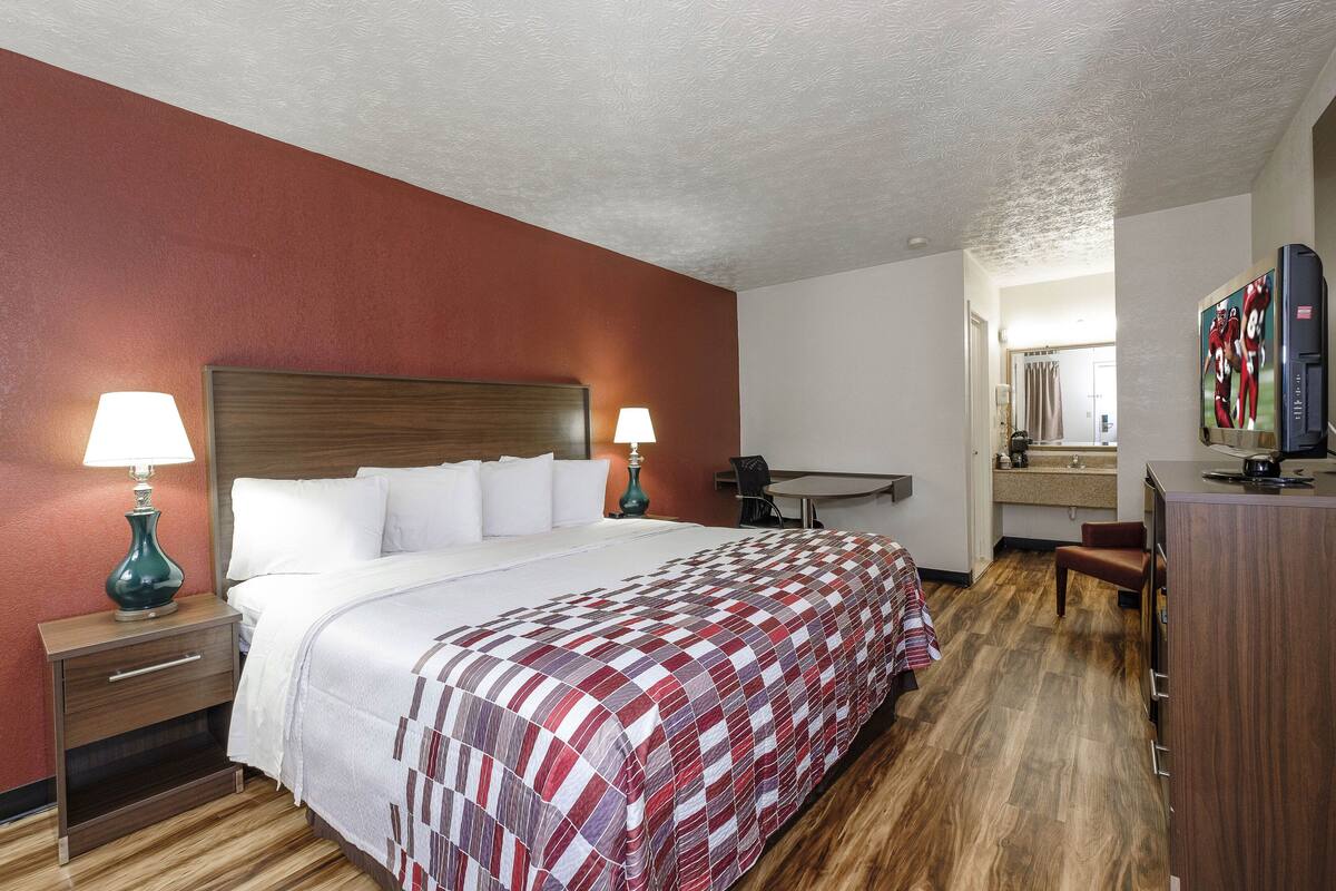 A hotel room with a large bed, two bedside tables with lamps, a desk, and a television.