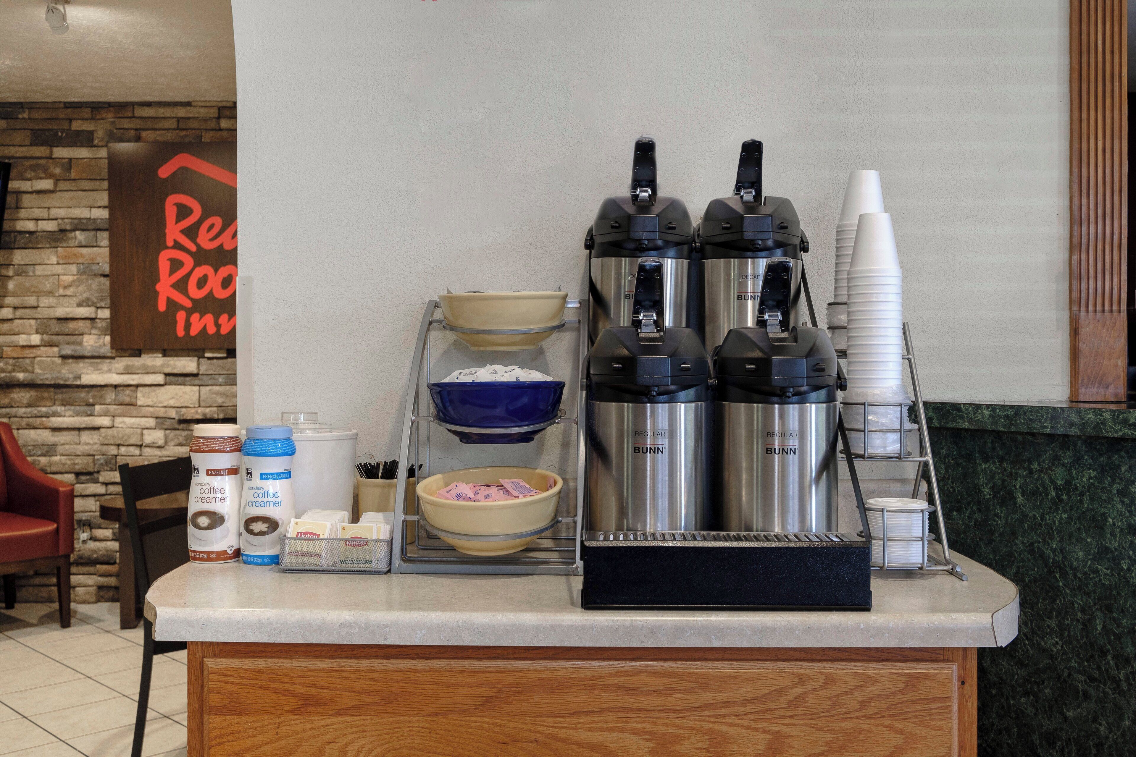 Kaffestation med kaffemaskine, dispensers til mælk og en skål med sukker.