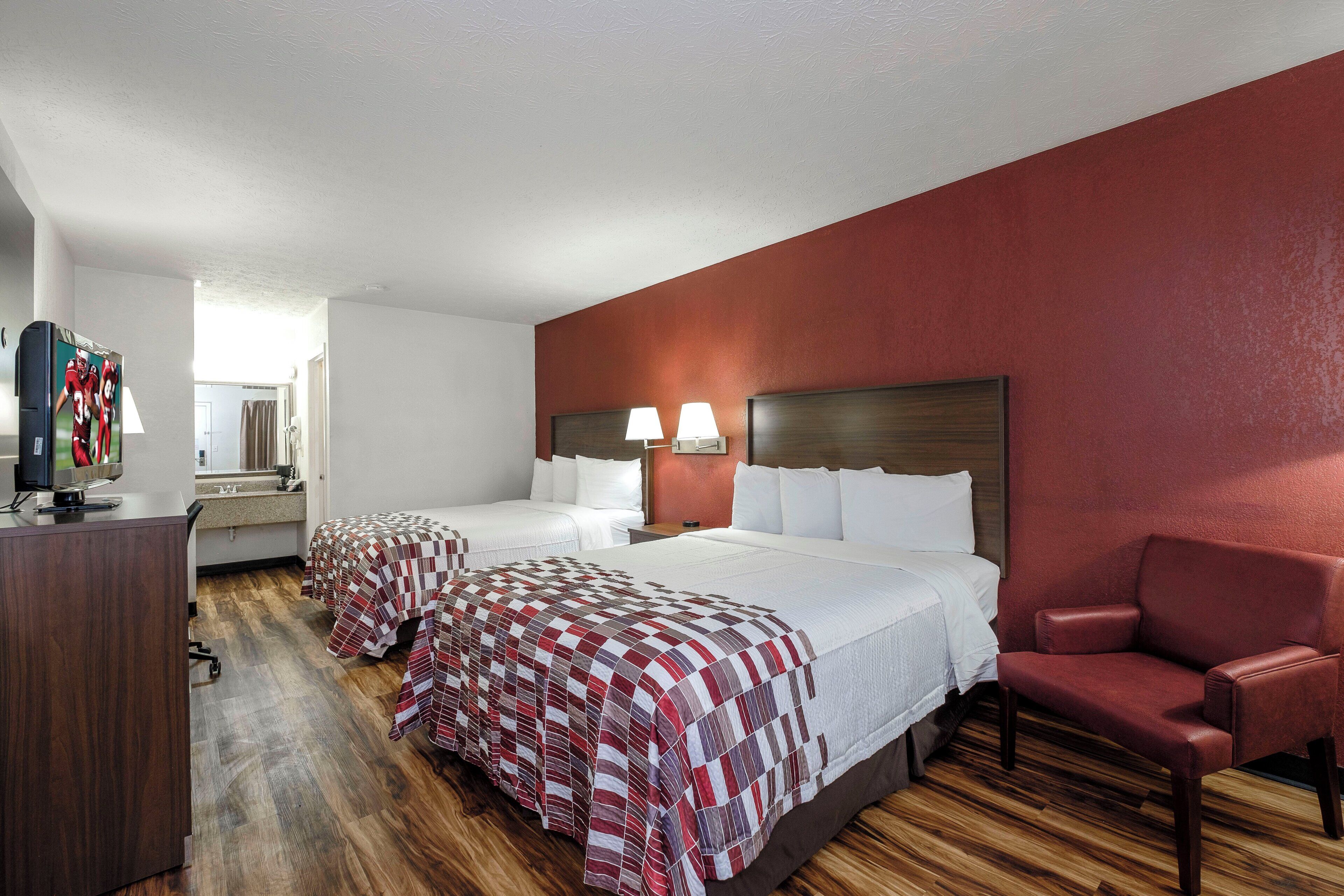 A hotel room with two beds, a desk, a chair, and a television.