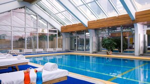 Una piscina interior con sillones de descanso, toallas y una bebida sobre una mesa.