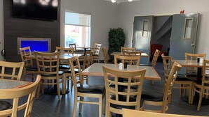 A dining area with multiple tables and chairs, a flat-screen TV mounted on the wall, and a staircase leading to another level. - Howard Johnson by Wyndham Oklahoma City Airport/ Fairgrounds (Oklahoma City)