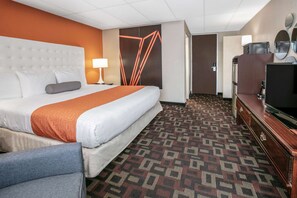 A hotel room with a large bed, a desk with a television, and a patterned carpet. - Howard Johnson by Wyndham Oklahoma City Airport/ Fairgrounds (Oklahoma City)