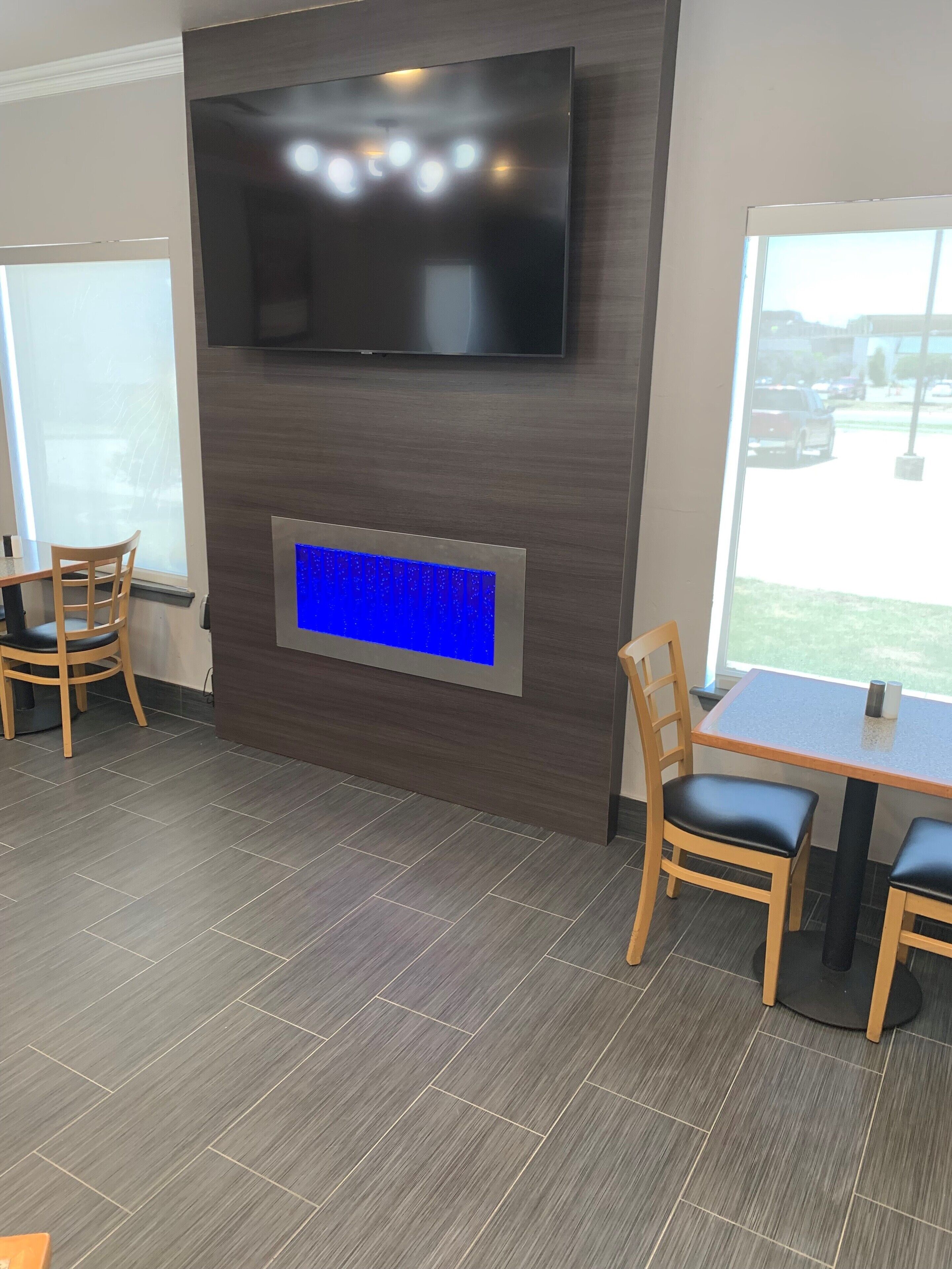 A modern interior with a flat-screen TV mounted on the wall, a blue illuminated panel below, and a dining area with wooden chairs and a table.