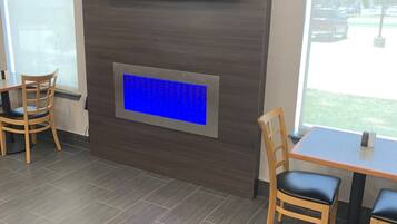 Un intérieur moderne avec un téléviseur à écran plat fixé au mur, un panneau bleu rétroéclairé en dessous, et un coin repas avec des chaises et une table en bois.