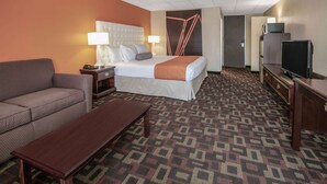 A hotel room with a bed, a sofa, a desk, a TV, and a patterned carpet. - Howard Johnson by Wyndham Oklahoma City Airport/ Fairgrounds (Oklahoma City)