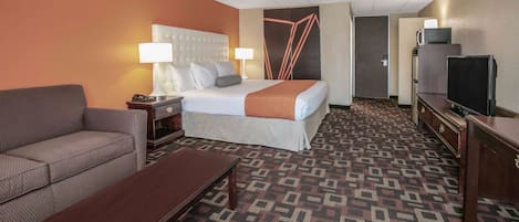 A hotel room with a bed, a sofa, a desk, a TV, and a patterned carpet.