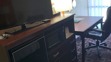 Quarto de hotel com televisão de tela plana, uma escrivaninha, uma cadeira e um abajur.
