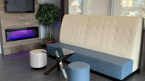 A modern living room with a sofa, a glass coffee table, a round ottoman, a flat-screen TV, and a fireplace with a purple light. - Howard Johnson by Wyndham Oklahoma City Airport/ Fairgrounds (Oklahoma City)
