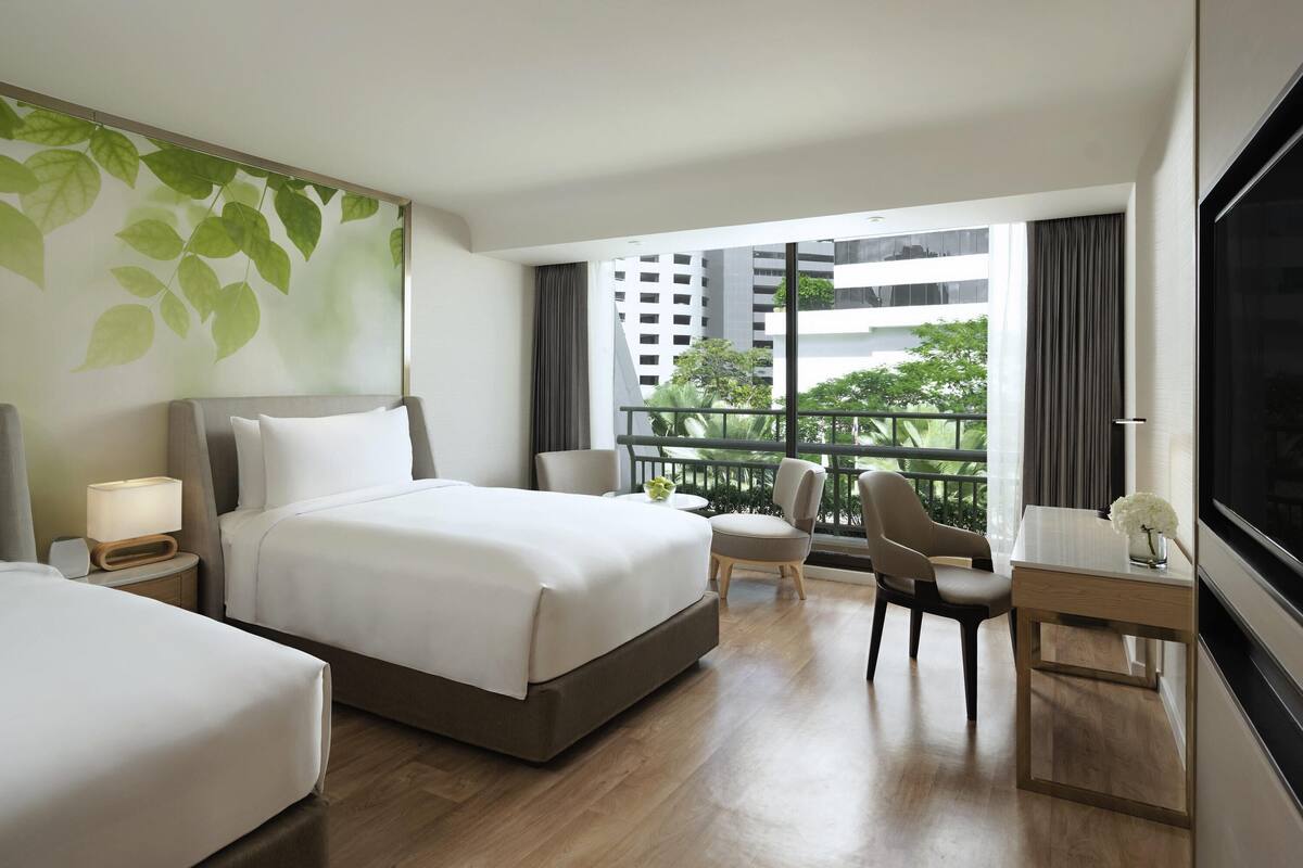 Ein modernes Hotelzimmer mit einem großen Bett, einem Schreibtisch und einem Stuhl. Ein Balkon bietet Blick auf die Stadt.