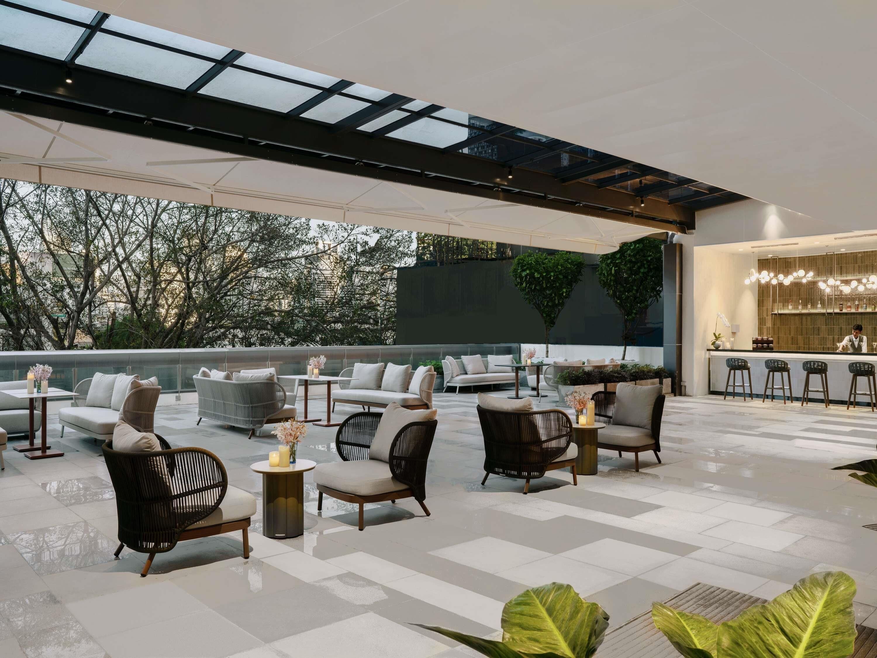 A rooftop lounge with outdoor seating, a bar area, and a view of trees and buildings.