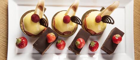 A white rectangular plate with three dessert items and four chocolate bars, each with a strawberry.