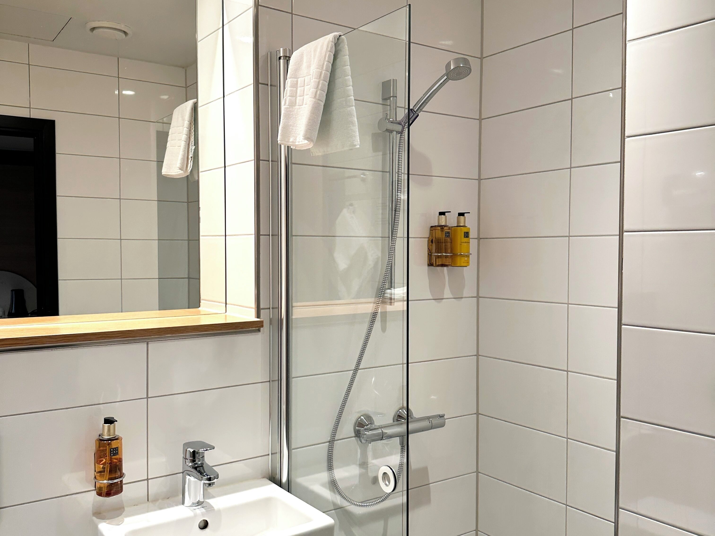 A modern bathroom with a glass-enclosed shower, a sink with a mirror, and toiletries on the wall.