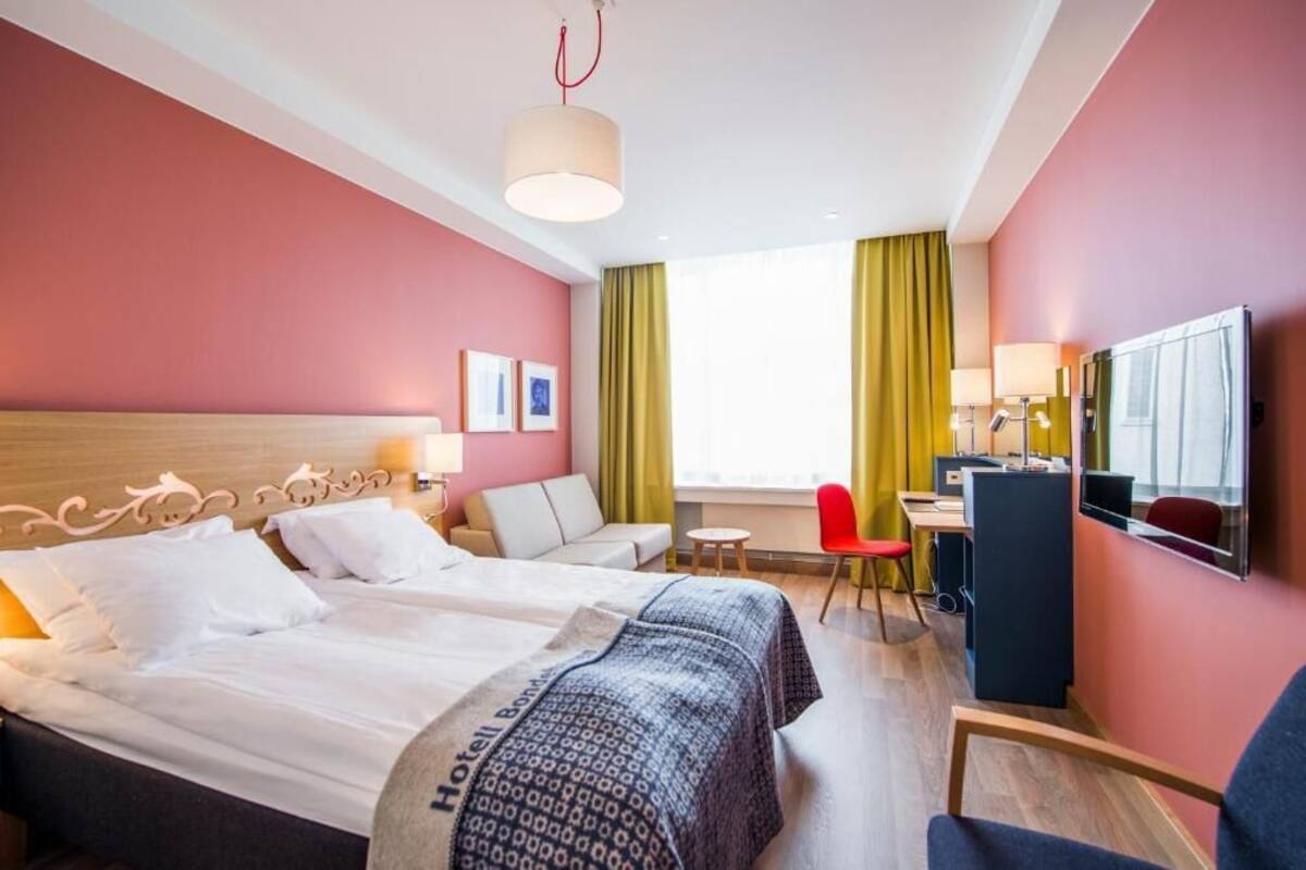 A hotel room with a bed, a desk, a chair, a TV, and a window with curtains.