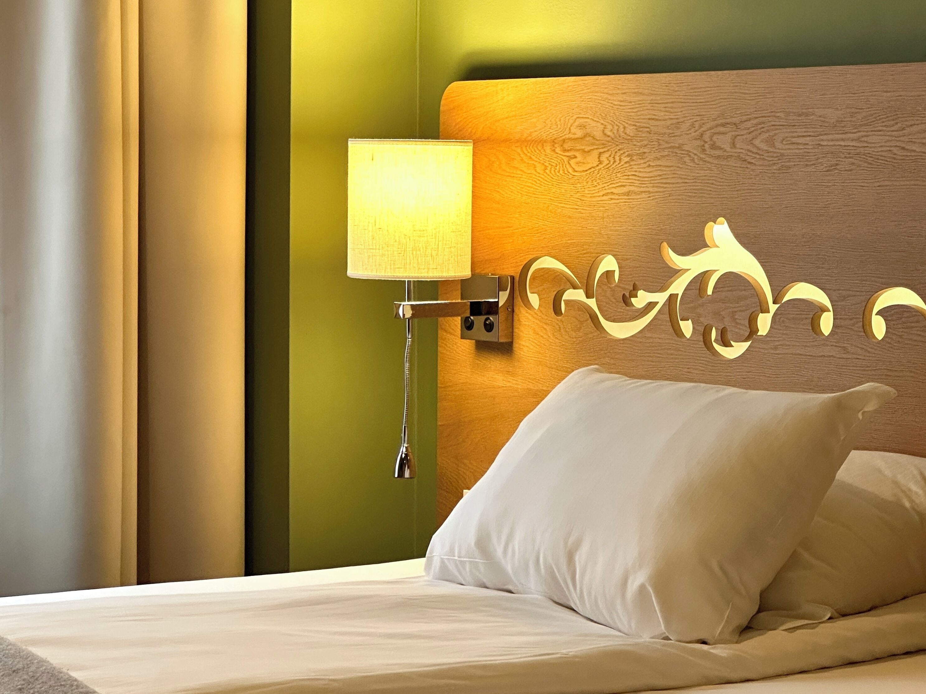 A hotel room with a bed, a nightstand with a lamp, and a decorative headboard.