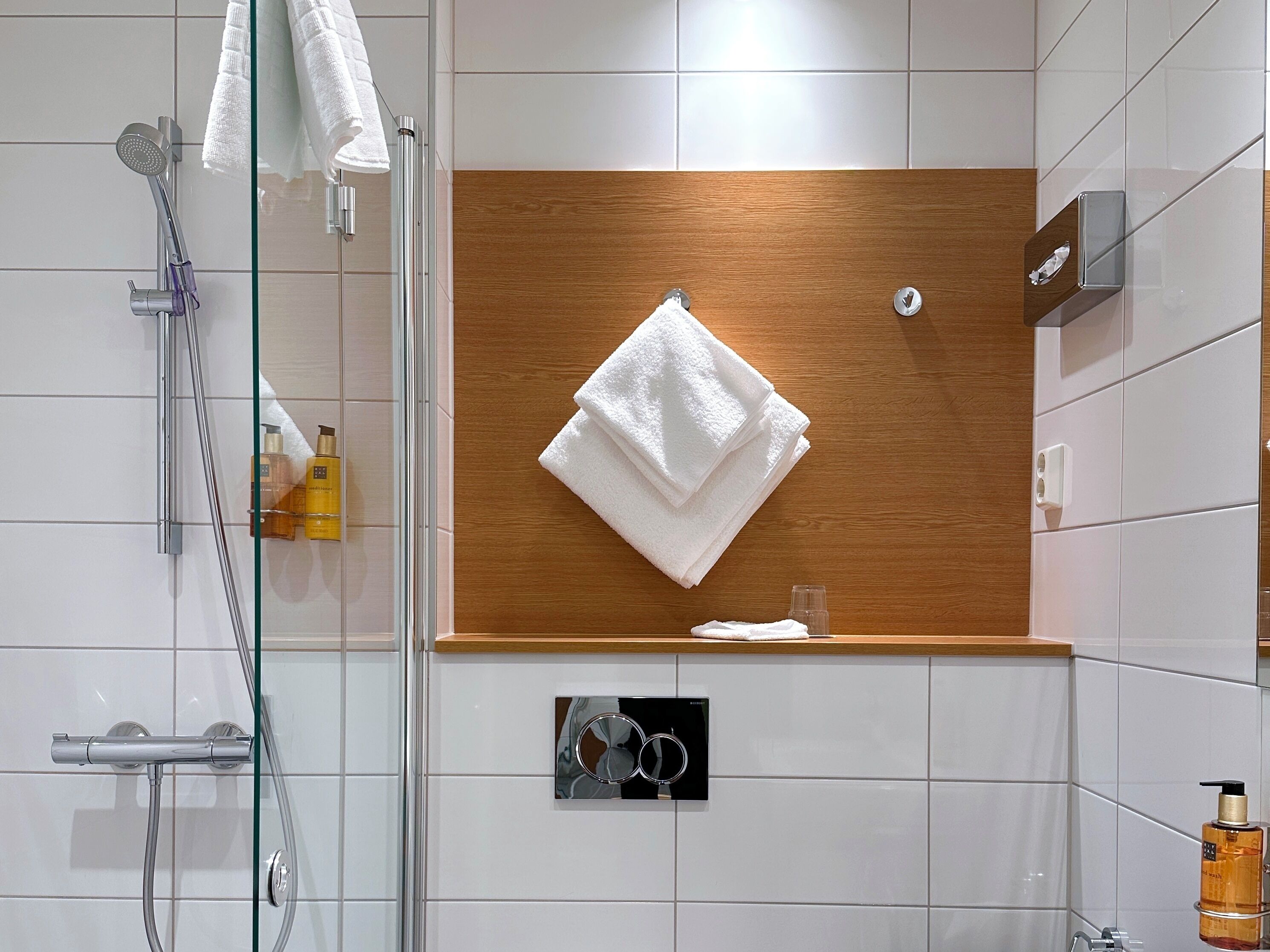 A modern bathroom with a glass shower enclosure, a wooden vanity with a towel rack, and toiletries.