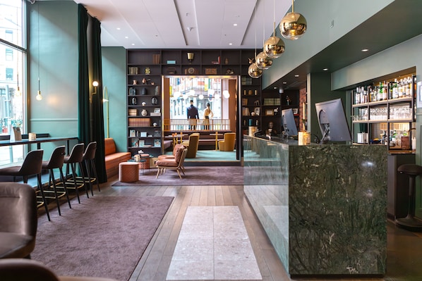 Un área de bar moderna con una barra de mármol, asientos con sillas acolchadas y vistas a la calle a través de amplios ventanales.