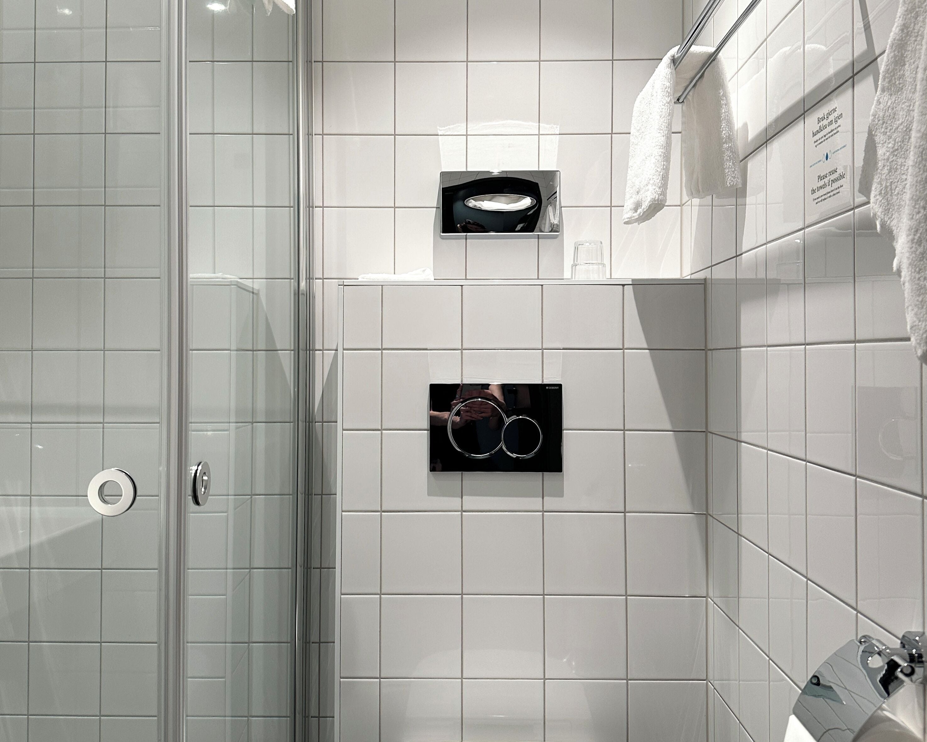 Un baño moderno con azulejos blancos, cabina de ducha de vidrio, toallero y secamanos.