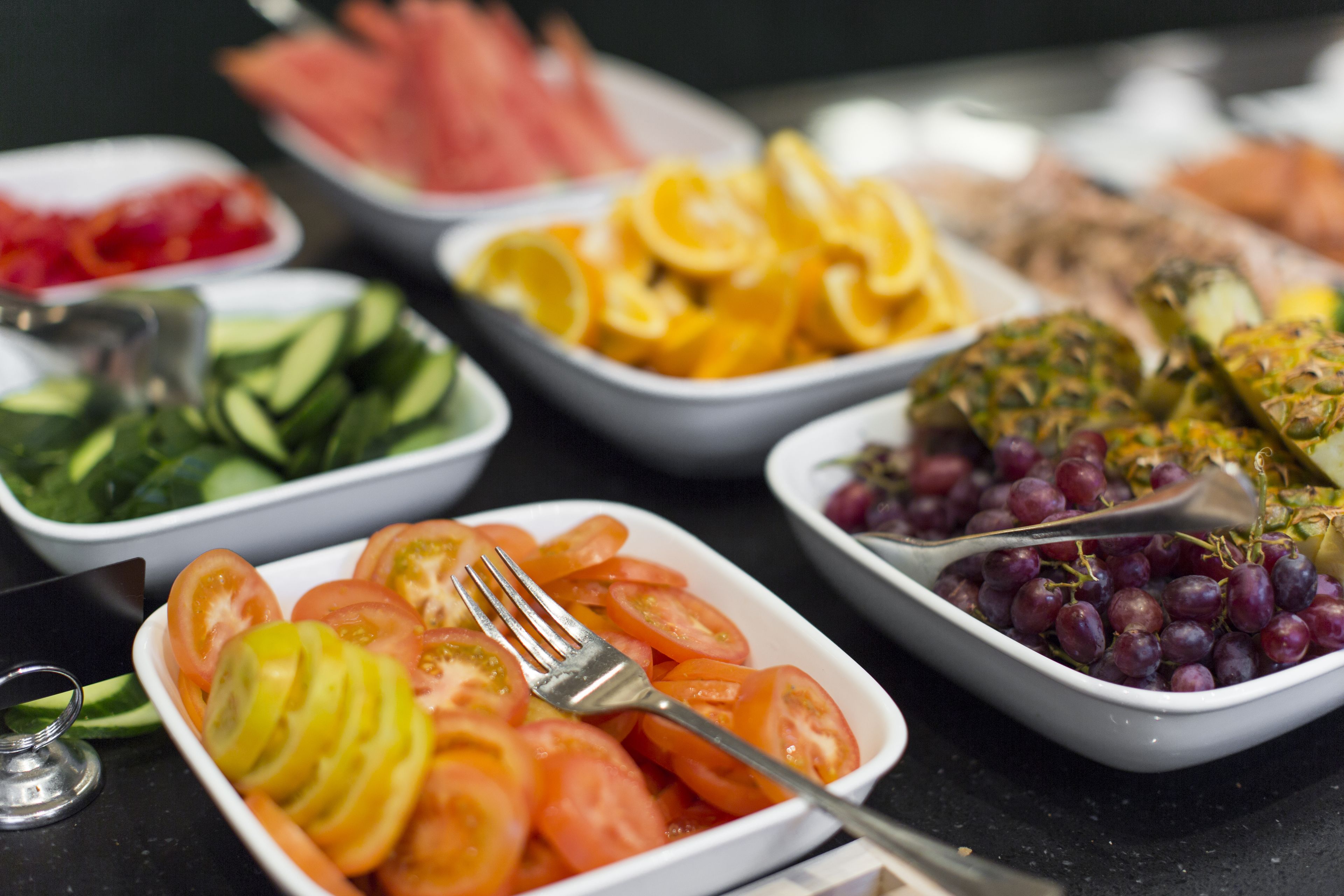 Diversos alimentos servidos en cuencos, como tomates en rodajas, pepinos y uvas.