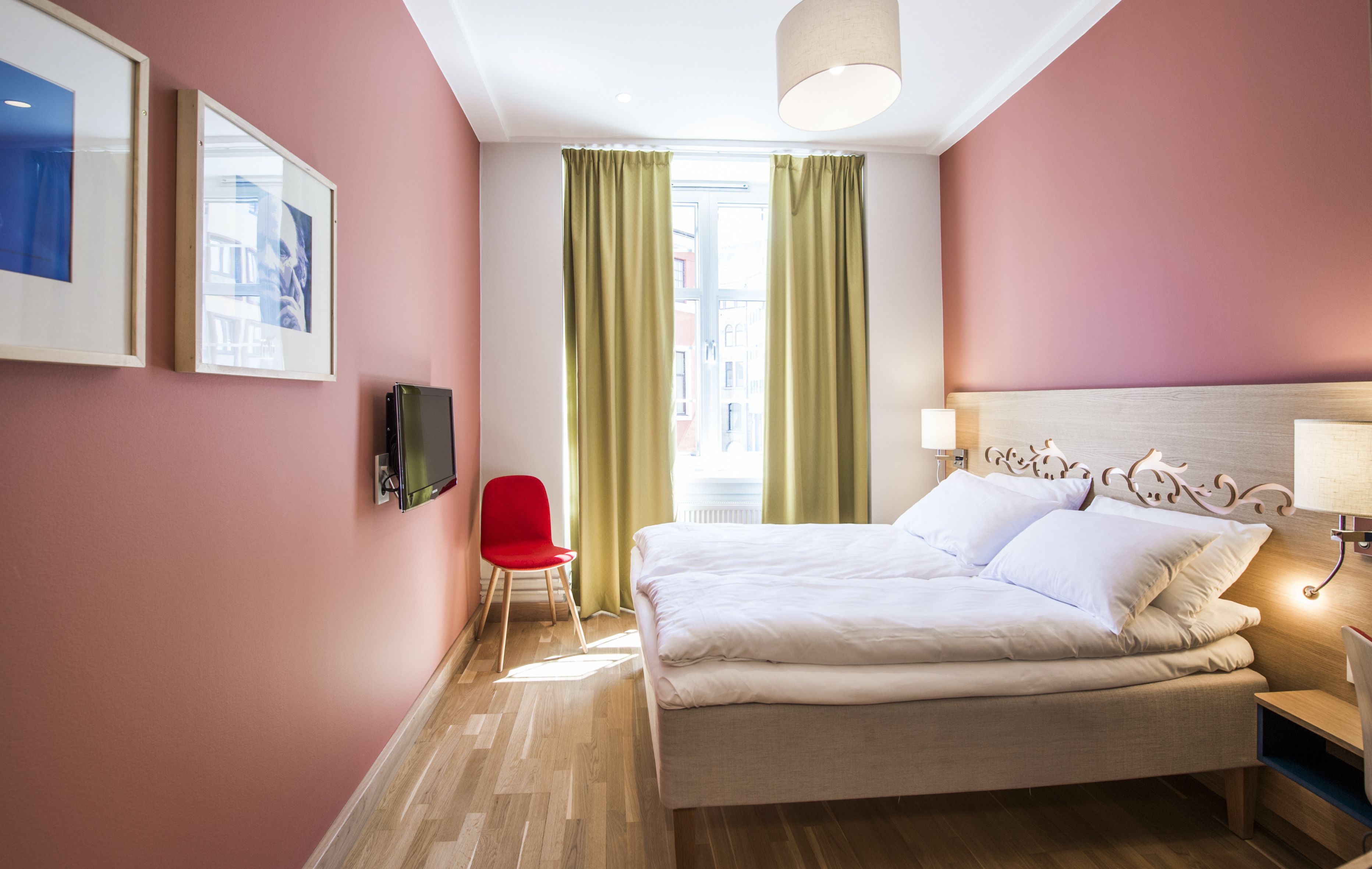 A hotel room with a bed, a TV, a red chair, and a window with curtains.