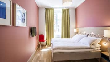 Una habitación de hotel con cama, televisión, una silla roja y ventana con cortinas.