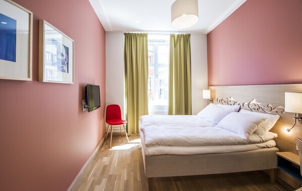 A hotel room with a bed, a TV, a red chair, and a window with curtains. - Hotell Bondeheimen (Oslo)