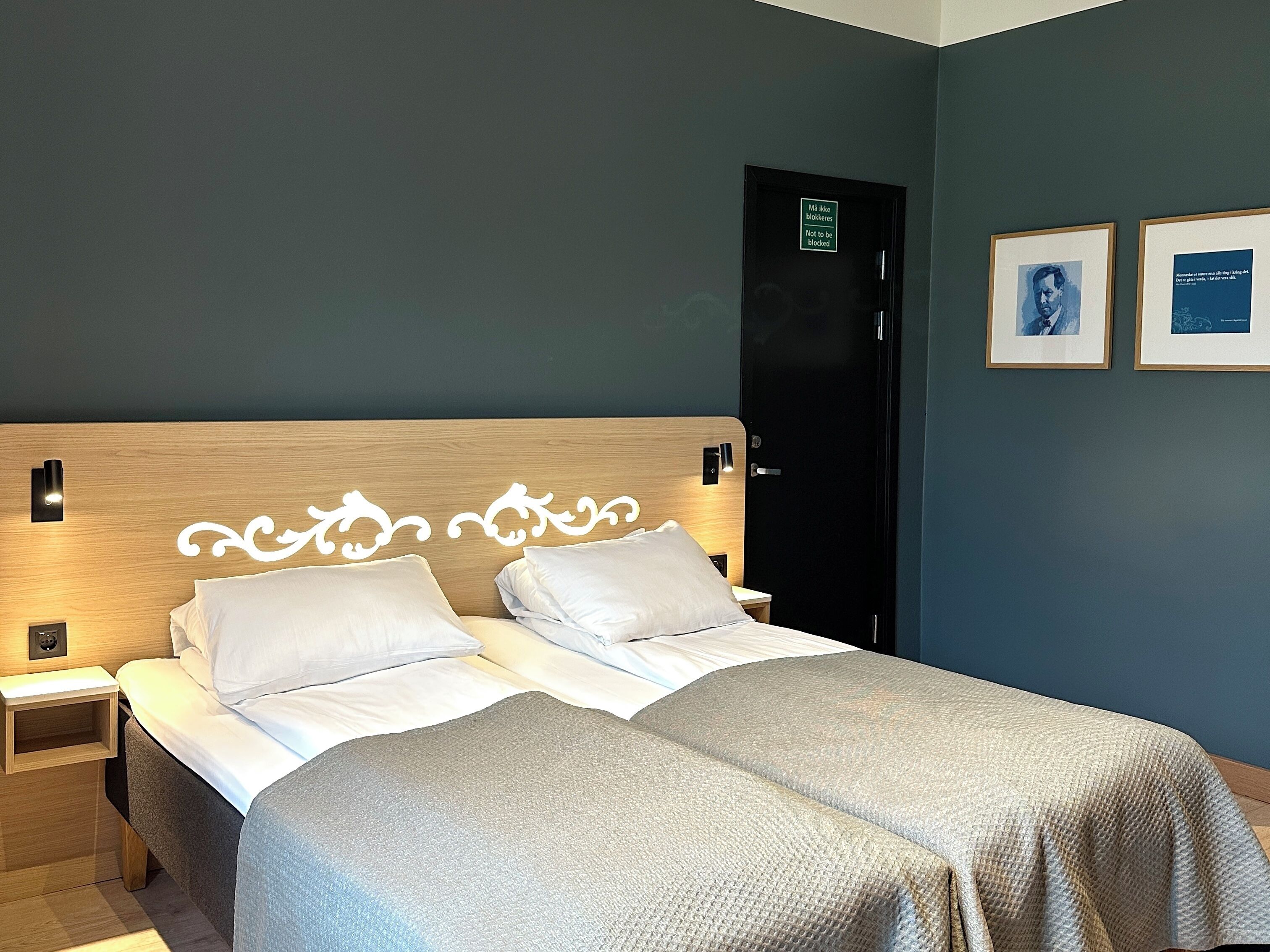 Una cama doble con sábanas blancas, cabecera de madera y manta gris.