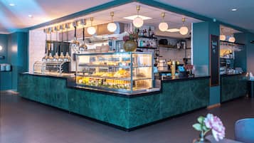 A well-lit bar area with a marble counter, a glass display case with food items, and hanging light fixtures.