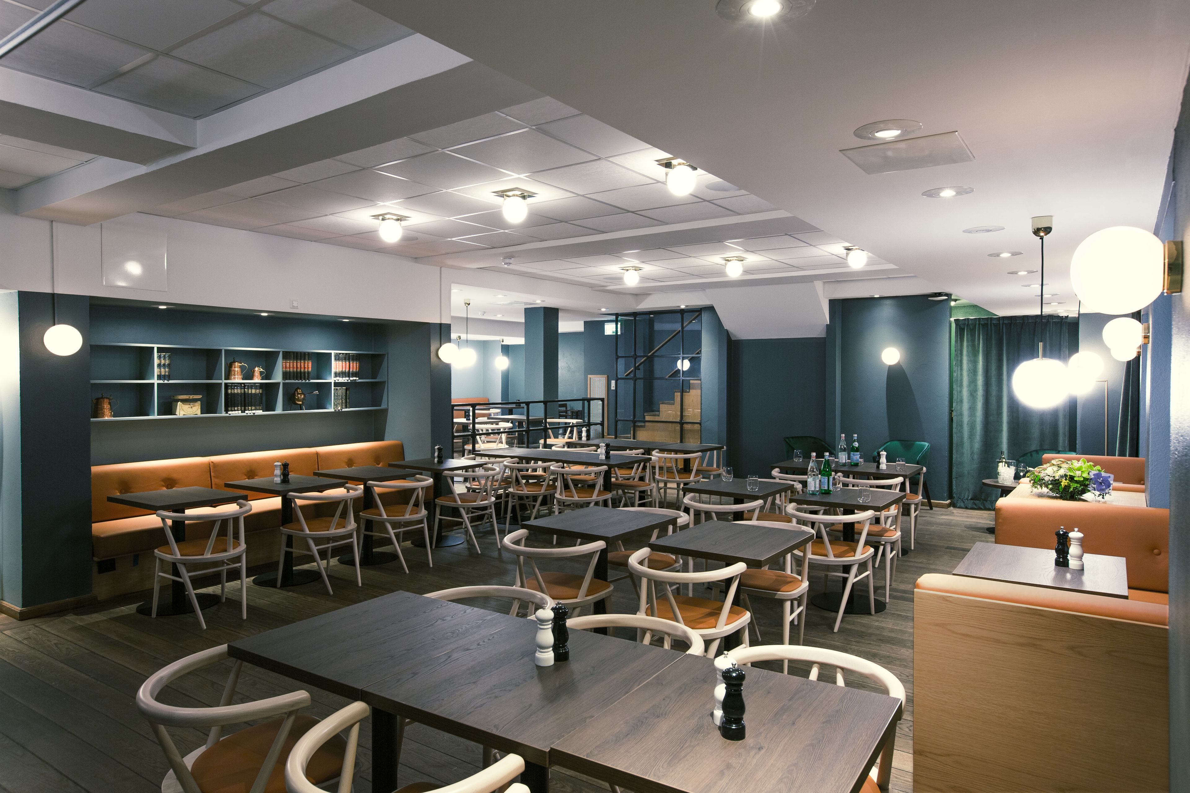 Un restaurante moderno con varias mesas y sillas, una zona de bar y una escalera que sube a un nivel superior.