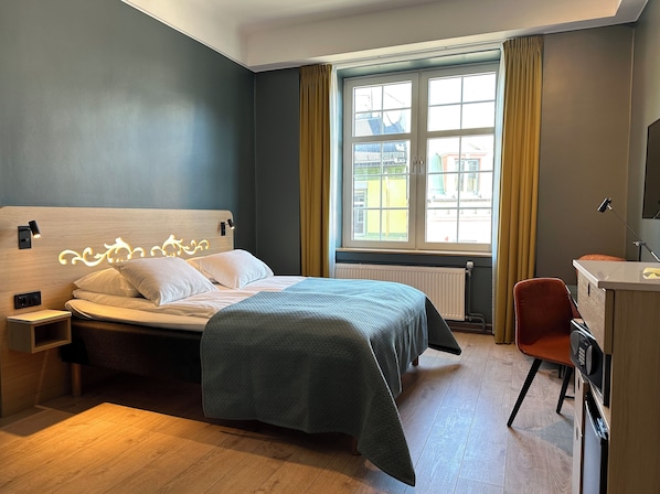 Una habitación de hotel moderna con cama, mesita de noche y escritorio con silla.