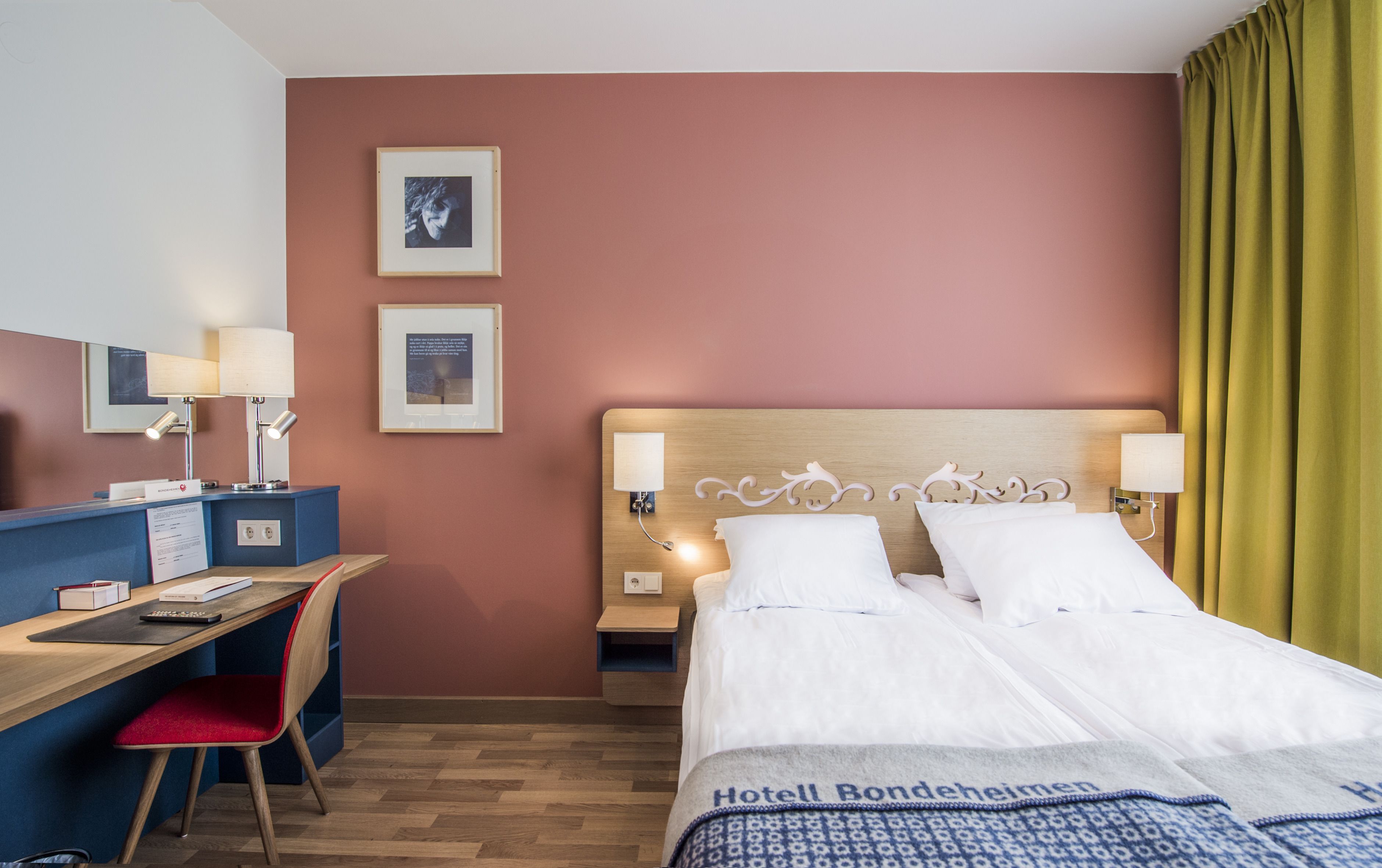 Habitación de hotel con cama, escritorio, silla y dos cuadros en la pared.