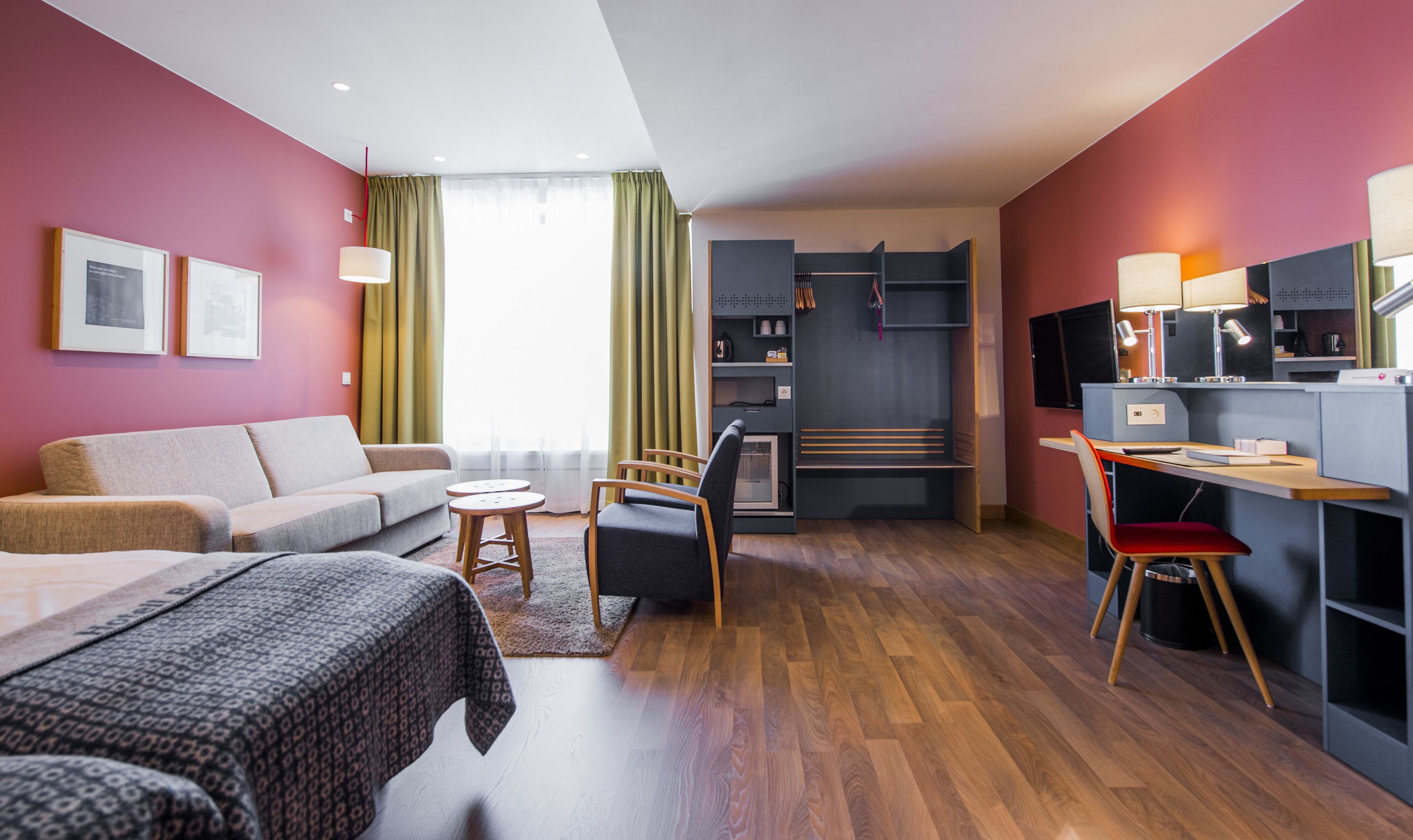 A modern hotel room with a sofa, a desk with a chair, a bed, and a TV.