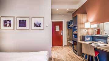 A hotel room with a bed, a desk with a chair, and three framed pictures on the wall.