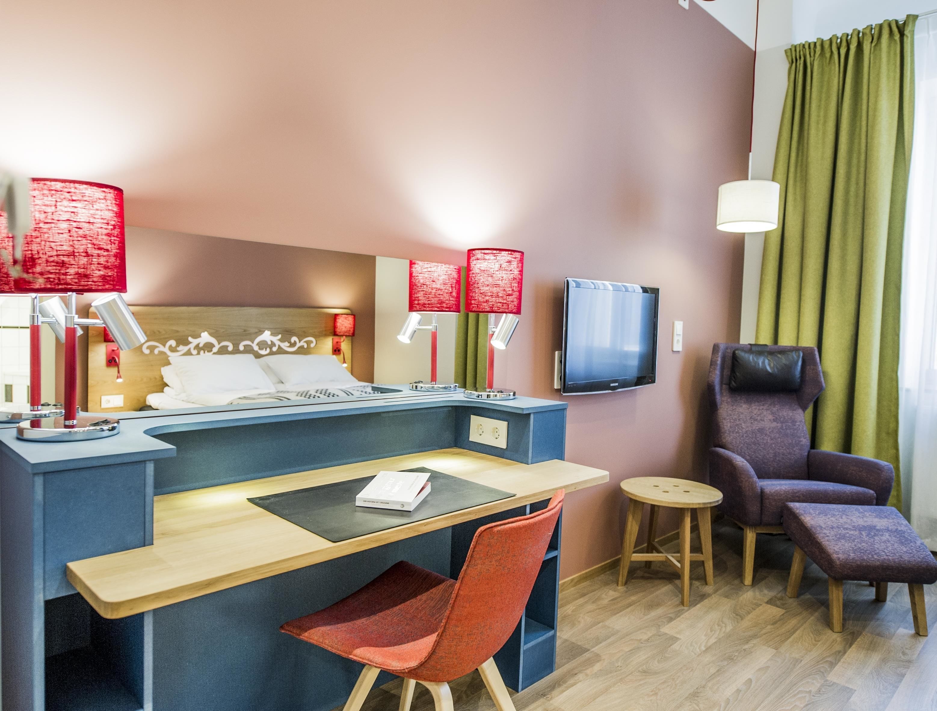 Une chambre d’hôtel équipée d’un lit, d’un bureau, d’une chaise, d’une télévision et d’une fenêtre avec des rideaux.