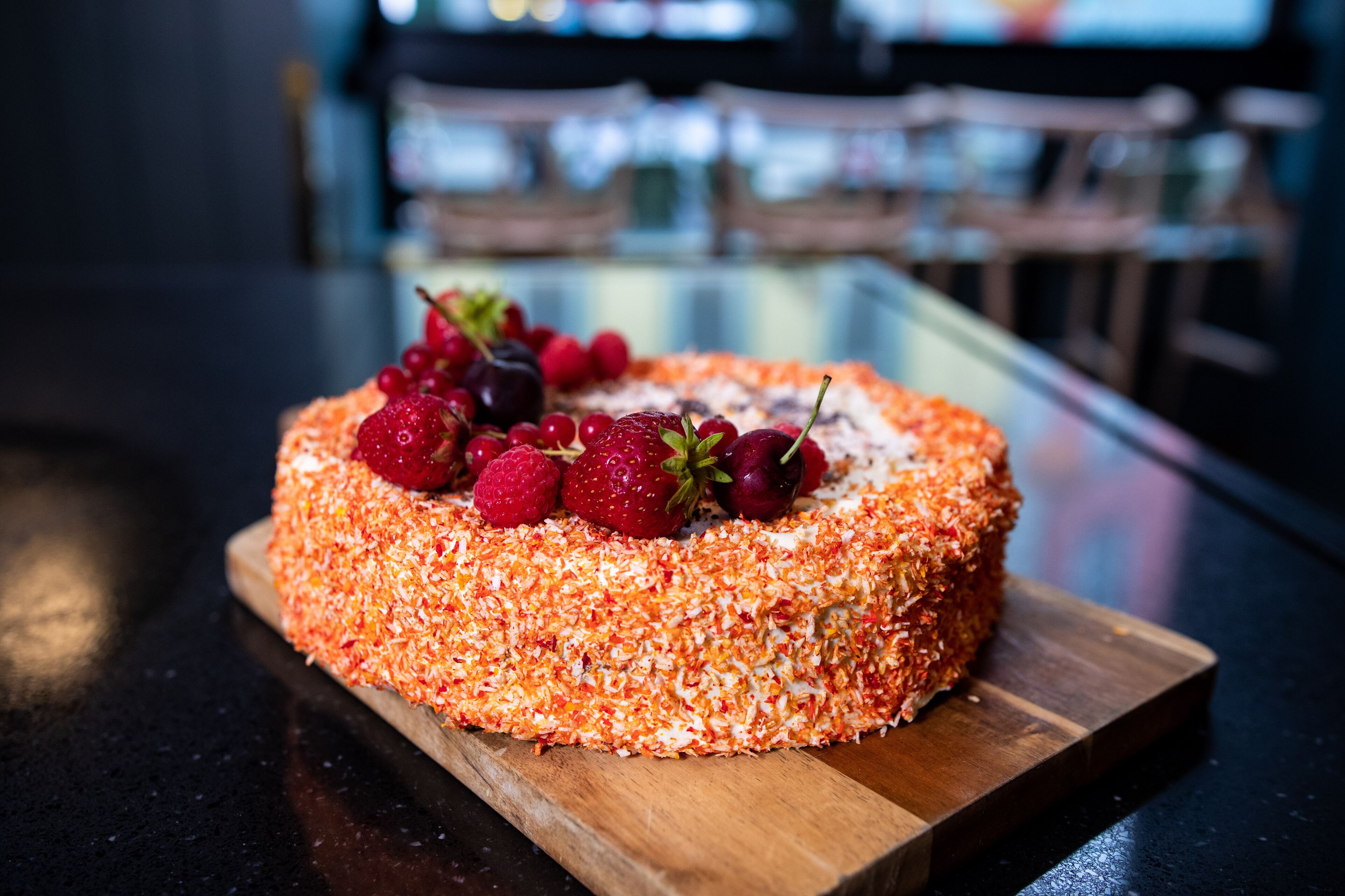 A round cake with a coconut topping and strawberries on a wooden board.