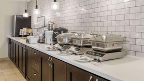 A modern kitchen with a white tiled backsplash, stainless steel appliances, and a buffet setup with food warming stations. - Best Western Plus Grand Manor Inn (Springfield)