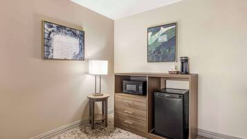 A compact hotel room with a kitchenette, a small table with a lamp, and two framed pictures on the walls.