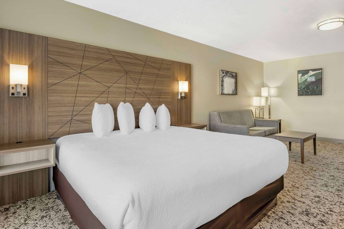 A hotel room with a large bed, a desk, a chair, and two wall-mounted lamps.